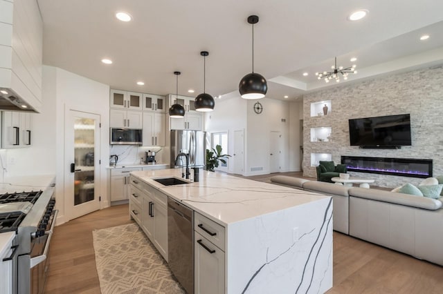 kitchen with a sink, open floor plan, white cabinetry, stainless steel appliances, and light wood-style floors