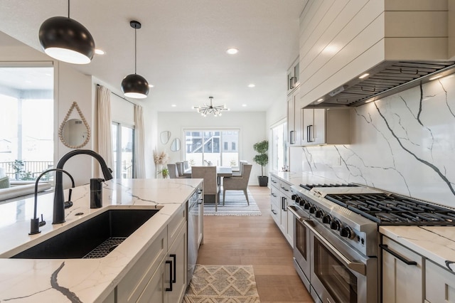 kitchen featuring custom exhaust hood, a sink, hanging light fixtures, decorative backsplash, and appliances with stainless steel finishes