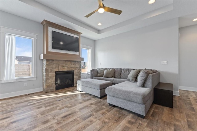 living room with a raised ceiling, wood finished floors, recessed lighting, a fireplace, and baseboards