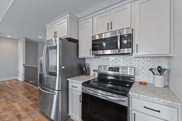 kitchen featuring backsplash, light stone counters, white cabinets, stainless steel appliances, and dark wood-style flooring