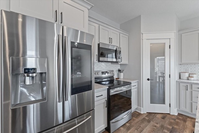 kitchen featuring light stone countertops, dark wood-type flooring, appliances with stainless steel finishes, white cabinetry, and backsplash