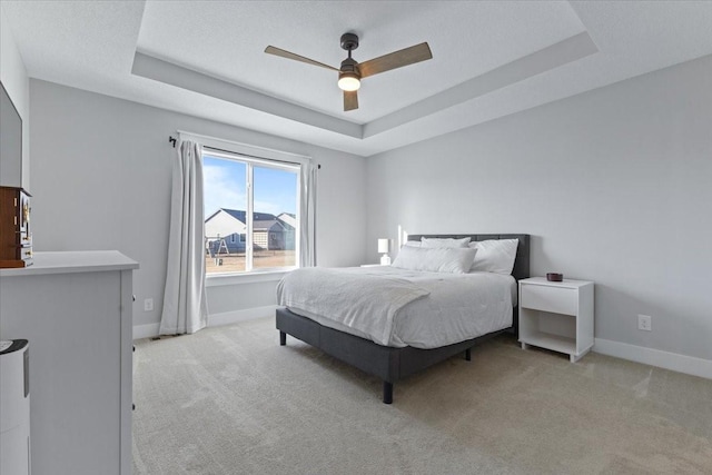 bedroom featuring a raised ceiling, baseboards, and light carpet