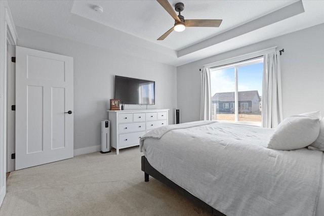 bedroom featuring a tray ceiling, light carpet, baseboards, and a ceiling fan