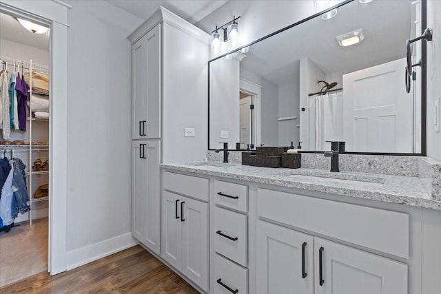 full bathroom with double vanity, a spacious closet, wood finished floors, and a sink