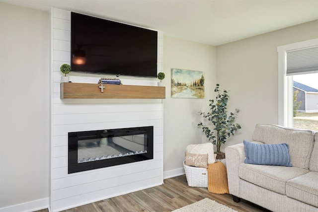 living area featuring wood finished floors, baseboards, and a large fireplace