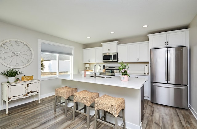 kitchen with a breakfast bar, an island with sink, a sink, appliances with stainless steel finishes, and light countertops