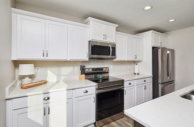 kitchen featuring recessed lighting, appliances with stainless steel finishes, white cabinetry, and light wood-style floors