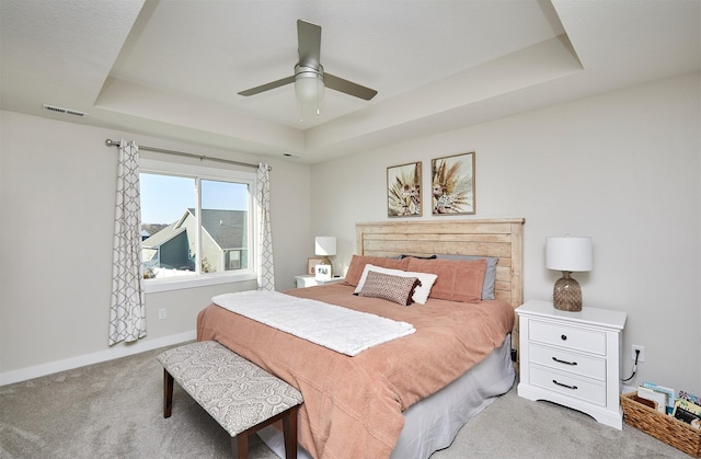 carpeted bedroom featuring a tray ceiling, baseboards, visible vents, and a ceiling fan