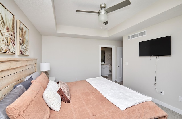 carpeted bedroom with visible vents, connected bathroom, baseboards, ceiling fan, and a tray ceiling