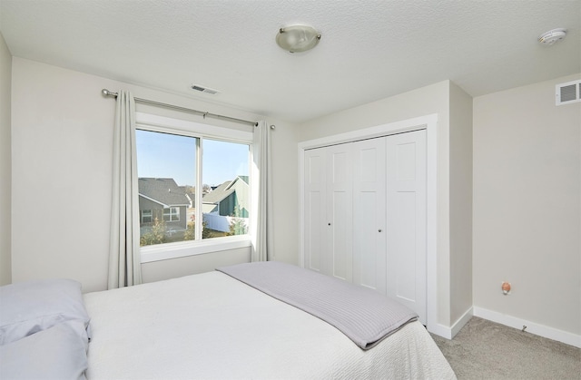 bedroom with visible vents, light carpet, a textured ceiling, a closet, and baseboards