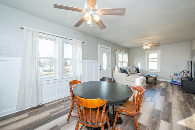 dining room with a decorative wall, wood finished floors, a wainscoted wall, and ceiling fan