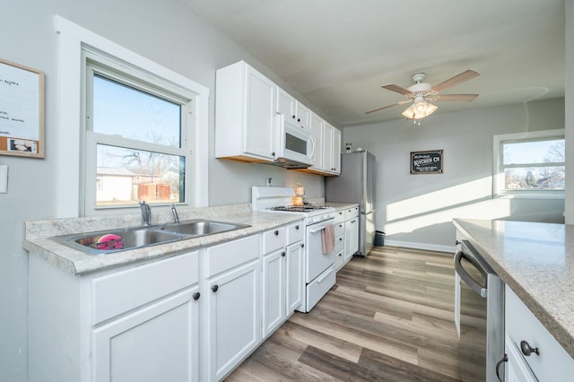 kitchen with ceiling fan, appliances with stainless steel finishes, light wood-style floors, white cabinets, and a sink