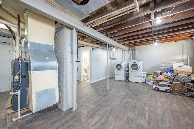 unfinished basement featuring concrete block wall, wood finished floors, and independent washer and dryer