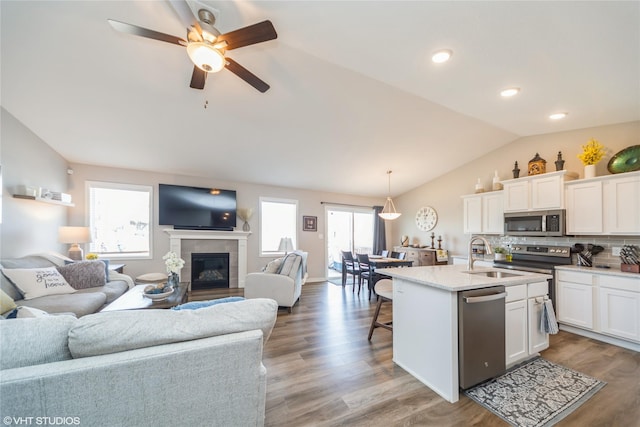 kitchen featuring open floor plan, lofted ceiling, white cabinets, stainless steel appliances, and a sink