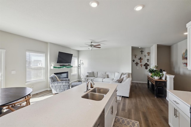 kitchen featuring a sink, dark wood-style floors, open floor plan, a glass covered fireplace, and white cabinetry