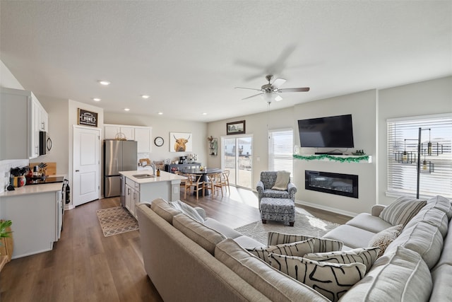 living room with a ceiling fan, recessed lighting, dark wood-type flooring, a textured ceiling, and a glass covered fireplace