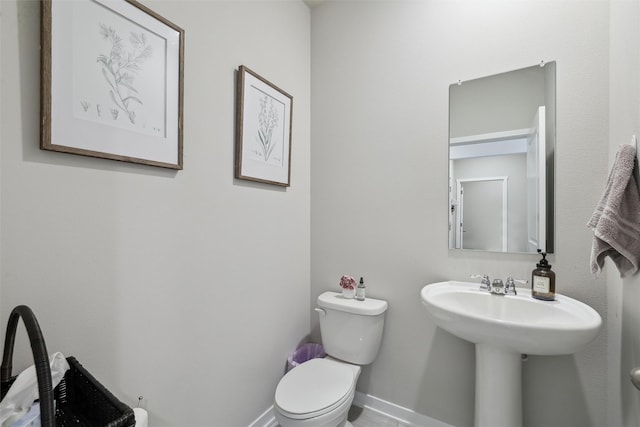 half bathroom featuring toilet, baseboards, and a sink