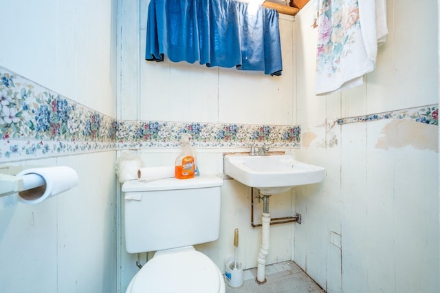 half bathroom with a sink, toilet, and wainscoting