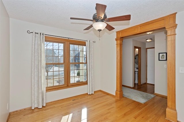 unfurnished room featuring decorative columns, light wood-style floors, baseboards, and a textured ceiling