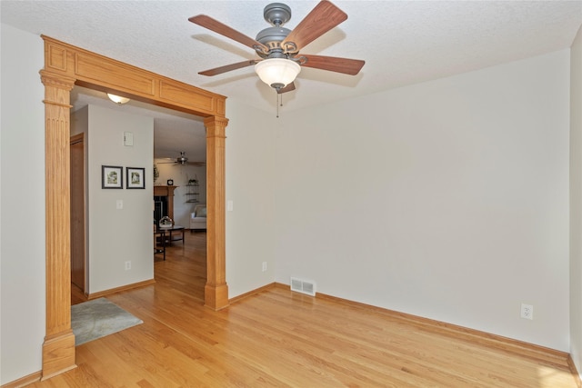 spare room featuring decorative columns, light wood-style floors, visible vents, and a textured ceiling