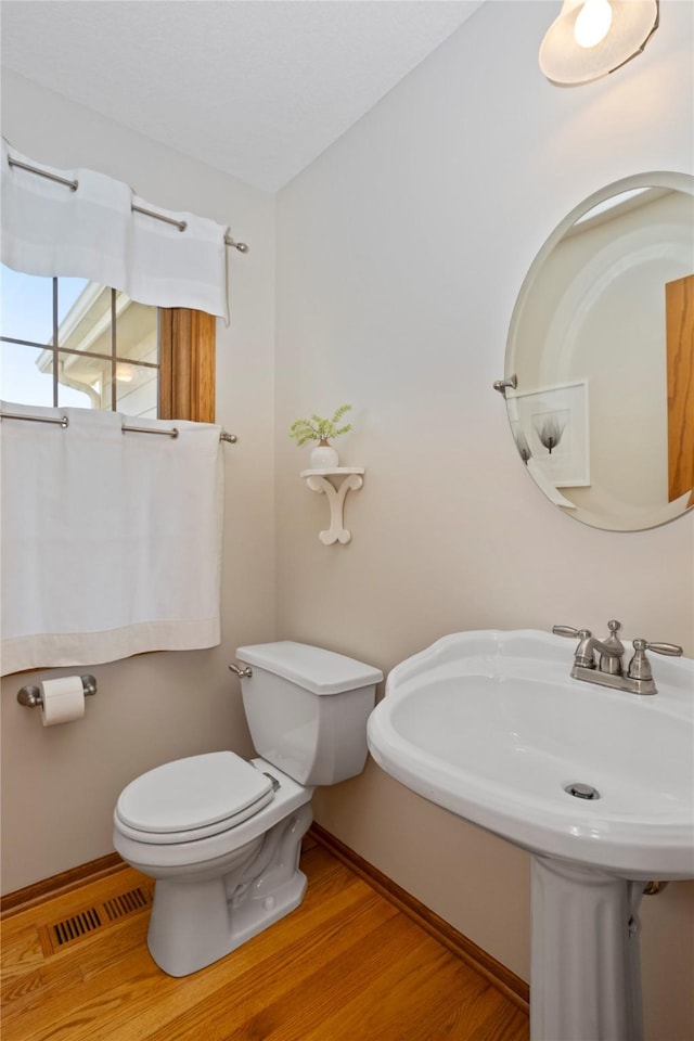 half bathroom with visible vents, toilet, a sink, wood finished floors, and baseboards