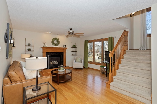 living area with stairway, a textured ceiling, wood finished floors, and a tiled fireplace