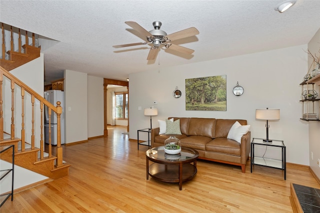 living room with light wood-style floors, ceiling fan, stairs, and a textured ceiling