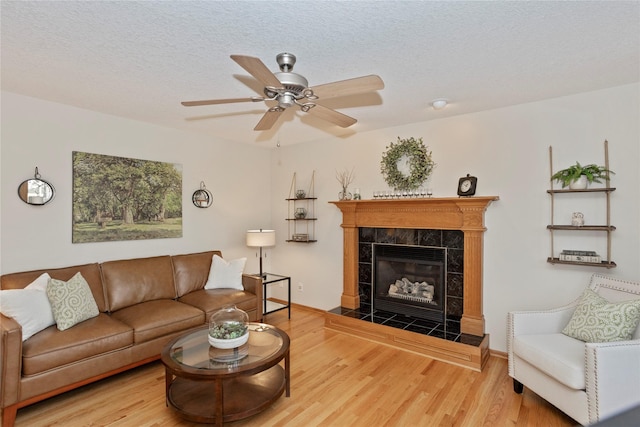 living area with baseboards, a tiled fireplace, wood finished floors, a textured ceiling, and a ceiling fan