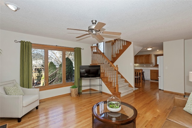 living room with baseboards, a textured ceiling, stairs, and light wood-style floors