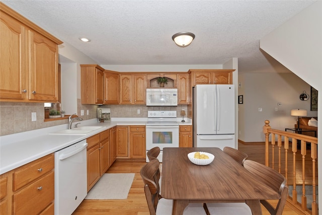 kitchen featuring light countertops, decorative backsplash, light wood-style flooring, white appliances, and a sink