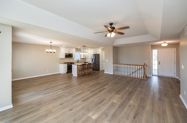 unfurnished living room with wood finished floors, baseboards, a sink, a raised ceiling, and ceiling fan with notable chandelier