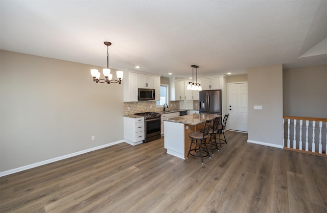 kitchen with a center island, a chandelier, decorative backsplash, appliances with stainless steel finishes, and white cabinetry