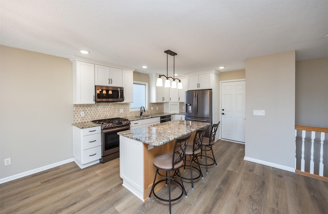 kitchen featuring a sink, a kitchen island, tasteful backsplash, white cabinetry, and appliances with stainless steel finishes