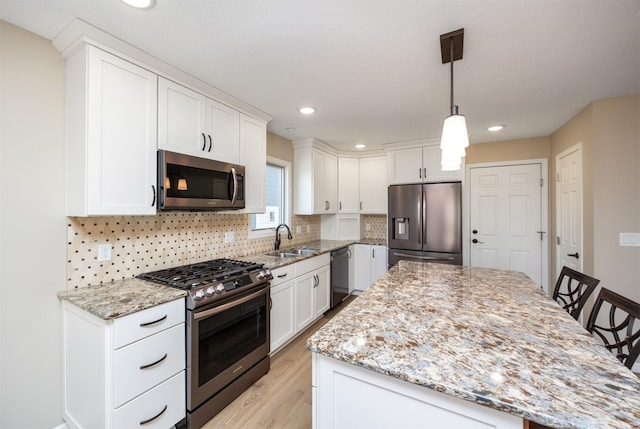 kitchen with a sink, decorative backsplash, stainless steel appliances, white cabinetry, and a center island