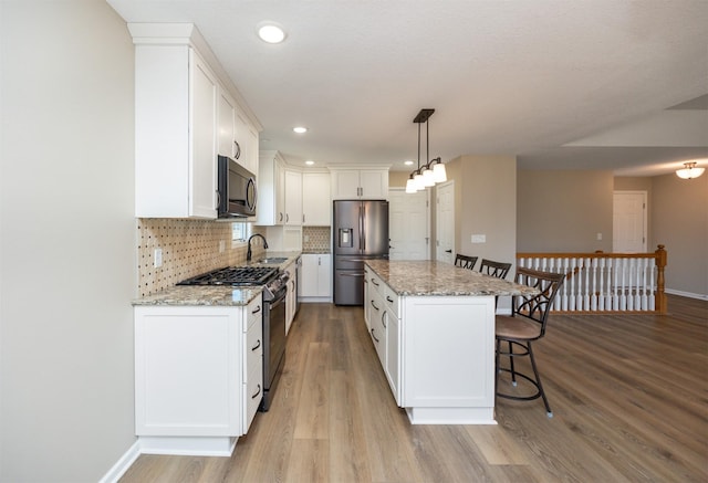 kitchen featuring a kitchen island, light wood-style flooring, stainless steel appliances, decorative backsplash, and a kitchen bar