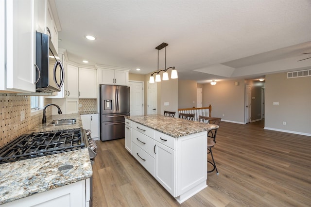 kitchen featuring light wood finished floors, visible vents, a kitchen bar, appliances with stainless steel finishes, and a sink