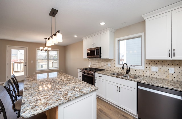 kitchen with a sink, appliances with stainless steel finishes, white cabinetry, tasteful backsplash, and a center island