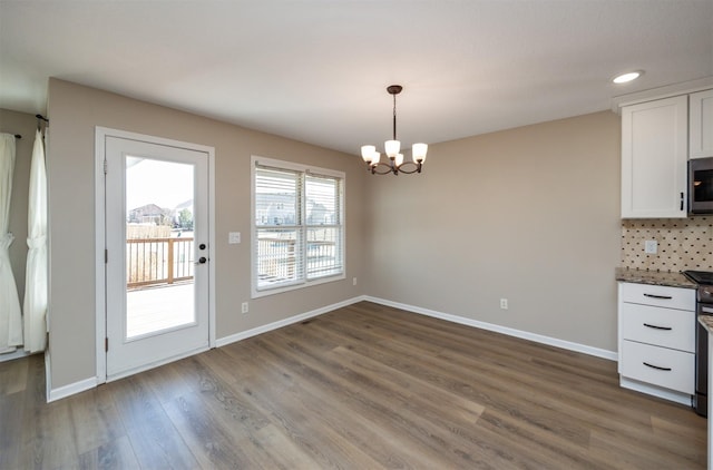 unfurnished dining area with an inviting chandelier, baseboards, and wood finished floors