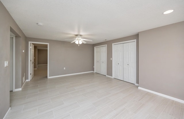 unfurnished bedroom with baseboards, multiple closets, a textured ceiling, and a ceiling fan