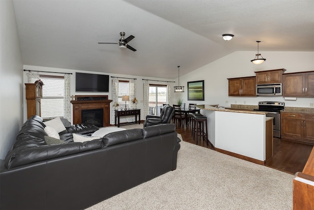 living area with ceiling fan, lofted ceiling, a glass covered fireplace, and dark wood-style floors