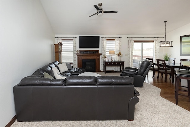 living room with wood finished floors, lofted ceiling, a glass covered fireplace, and a ceiling fan