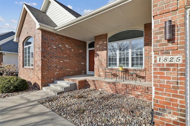 property entrance featuring brick siding, covered porch, and a shingled roof