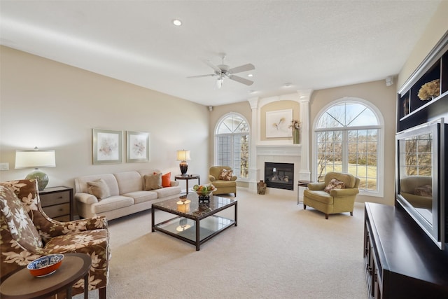 living area featuring a tiled fireplace, a healthy amount of sunlight, decorative columns, and carpet floors