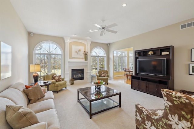 carpeted living area with visible vents, plenty of natural light, a glass covered fireplace, and a ceiling fan