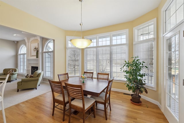 dining area featuring light wood-style flooring, baseboards, a wealth of natural light, and a large fireplace