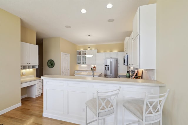 kitchen featuring glass insert cabinets, appliances with stainless steel finishes, a peninsula, light wood-style floors, and white cabinets