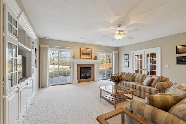 living room with light carpet, a textured ceiling, french doors, ceiling fan, and a tile fireplace