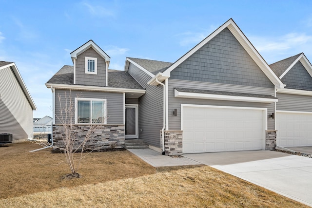 view of front of home featuring a shingled roof, concrete driveway, a front yard, central AC unit, and stone siding