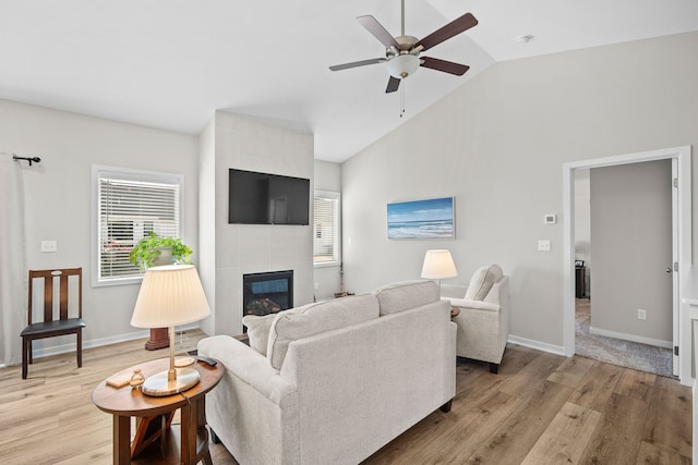 living area with baseboards, vaulted ceiling, light wood-style flooring, a tile fireplace, and a ceiling fan