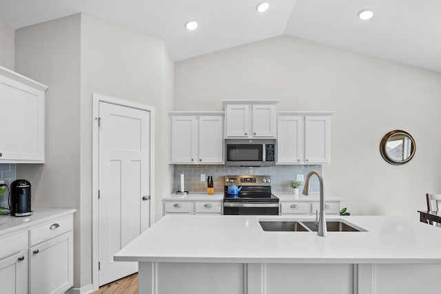 kitchen with light countertops, vaulted ceiling, appliances with stainless steel finishes, white cabinets, and a sink